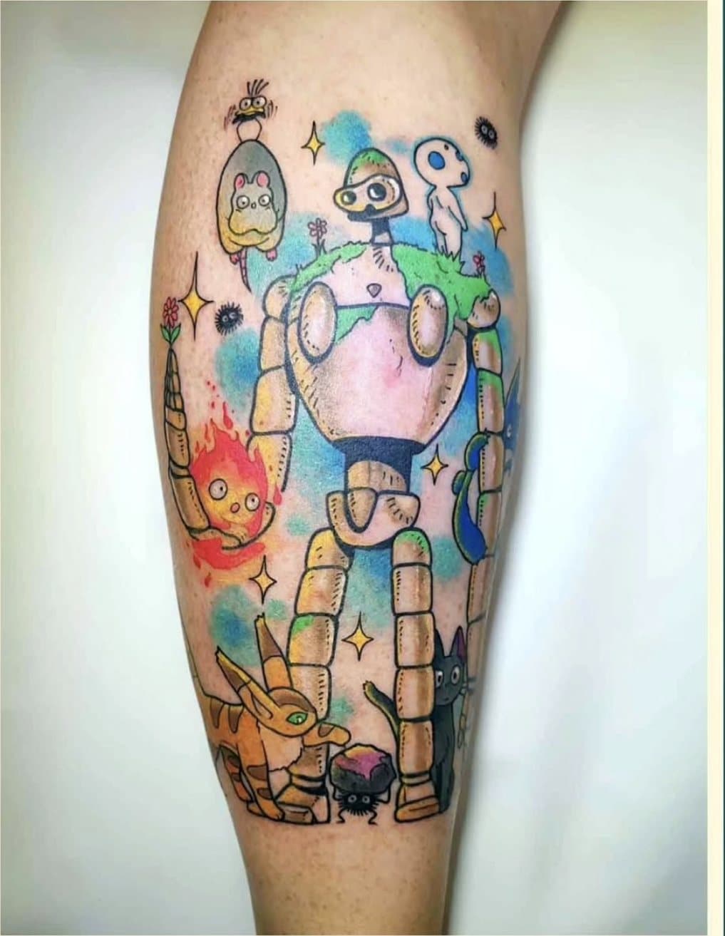 Tatouage couleur sur le mollet : un robot géant entouré de personnages inspirés de l'univers Ghibli, sur fond d'aquarelle bleue