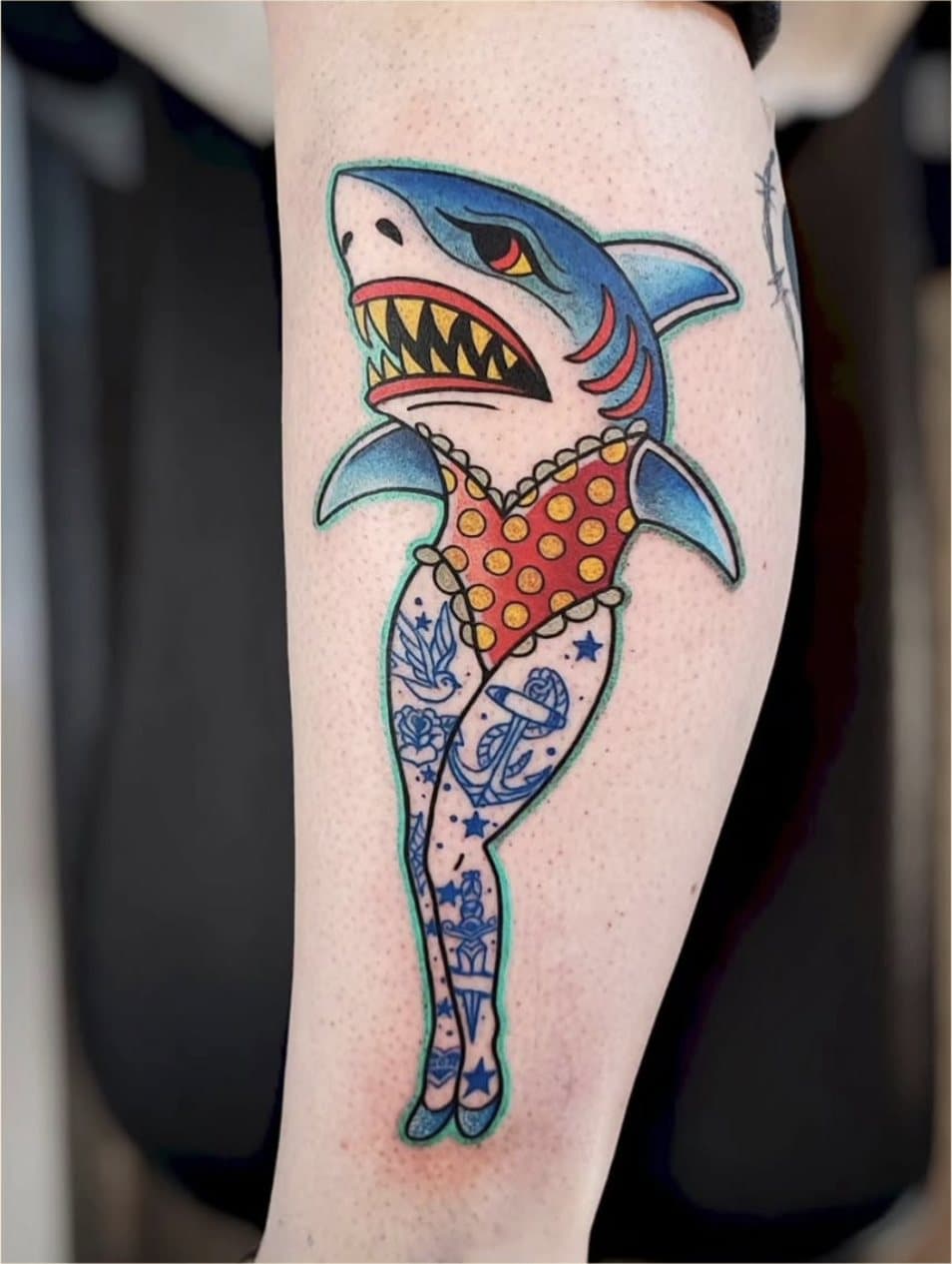 Tatouage couleur sur le mollet : un requin pin-up en maillot rouge à pois jaunes, jambes tatouées d'ancres et d'hirondelles